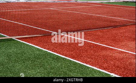 Dieses Bild fängt die lebendigen Details eines künstlichen Tennisplatzes ein und zeigt eine rote Spielfläche im Kontrast zu einer üppigen grünen Außengrenze Stockfoto