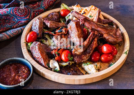 Eine Auswahl an saftigem, gegrilltem Fleisch einschließlich Rippchen und Steak, ergänzt durch frische Kirschtomaten und gegrilltes Gemüse, serviert auf einem rustikalen Wald Stockfoto