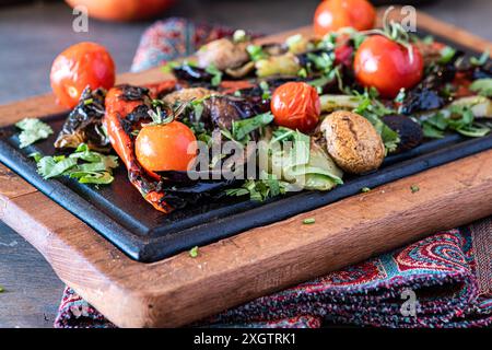 Eine lebendige Auswahl an gegrilltem Gemüse, einschließlich Paprika, Pilzen und Auberginen, garniert mit frischer Petersilie und serviert auf einem dunklen Holzschnitt Stockfoto