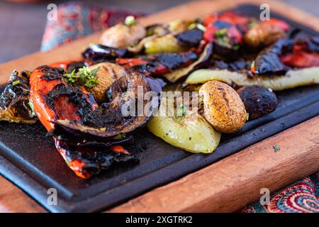 Eine lebendige Auswahl an gegrilltem Gemüse, einschließlich Paprika, Pilzen und Auberginen, präsentiert auf einer dunklen Holzserviertafel, abgeschmeckt mit fr Stockfoto