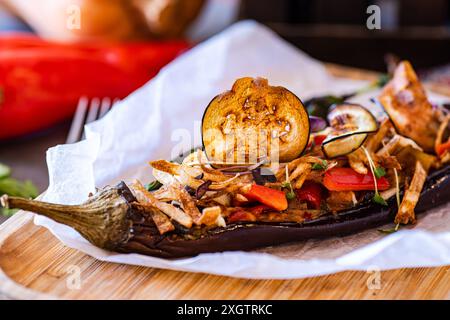 Gourmet-Gericht mit einer gefüllten Aubergine mit Kirschtomaten, Paprika, Zwiebeln, Knoblauch und Kartoffelscheiben, garniert mit Käse, serviert mit gar Stockfoto