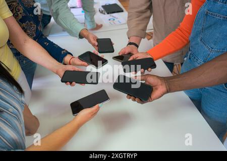 Eine nicht wiedererkennbare multikulturelle Gruppe von Fachleuten, die an einem Tisch stehen und auf Smartphones in einer modernen Büroumgebung zeigen Stockfoto