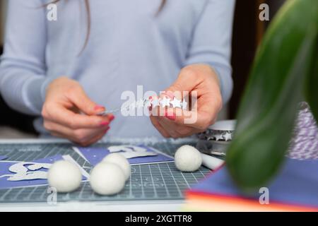 Die anonyme junge Frau konzentriert sich darauf, ein charmantes Papierwerk herzustellen, indem sie feine sternförmige Ausschnitte mit Präzision herstellt. Dieses Bild erfasst Nahaufnahmen Stockfoto