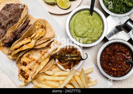 Ein Blick von oben auf ein traditionelles mexikanisches hausgemachtes Gericht mit gegrilltem Steak auf Maistortillas, begleitet von Guacamole, Salsa roja, karamelisierten Zwiebeln, Stockfoto