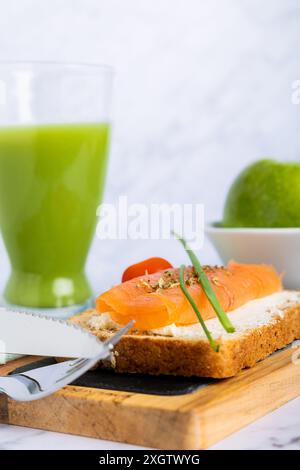 Blick von oben auf eine gesunde Mahlzeit mit einem Lachssandwich auf Mehrkornbrot mit Frischkäse, garniert mit Schnittlauch, frischer Gurke und Apfel-j Stockfoto