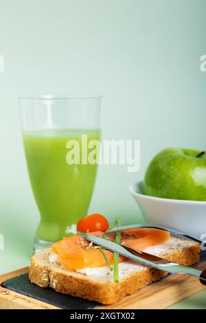 In einem lebendigen Display zeigt dieses Bild ein gesundes Frühstück mit einem Glas frischer Gurke und Apfelsaft sowie einem Lachssandwich auf Multi Stockfoto