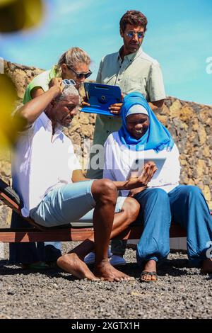Eine vielfältige Gruppe von vier Erwachsenen untersucht ein digitales Tablet in sonniger Umgebung. Die Gruppe besteht aus einem afrikanischen Mann, der sitzt, einer afrikanischen Frau mit Stockfoto