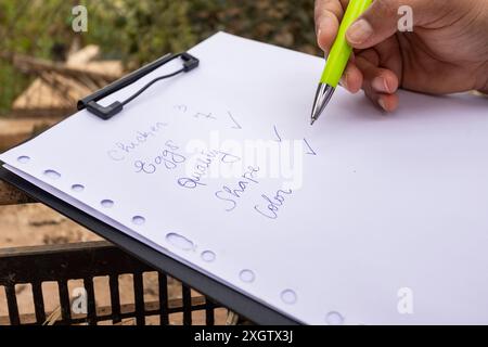 Nahaufnahme einer Hand einer zugeschnittenen, nicht erkennbaren Person, die eine Checkliste für den Betriebsbestand in die Zwischenablage schreibt. Die Liste zeichnet die Mengen sorgfältig auf Stockfoto