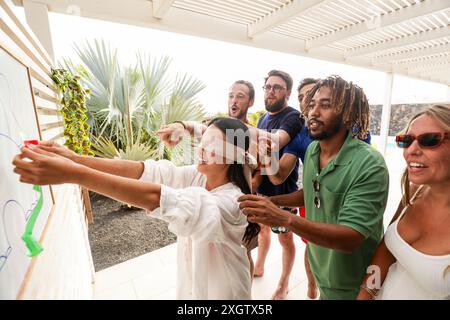 Eine vielfältige Gruppe von Freunden genießt ein verspieltes Spiel mit Augenbinde im Freien, bei dem die Essenz von Sommerspaß und Freundschaft unter einem sonnigen Himmel festgehalten wird. Stockfoto