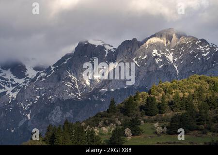 Ein dramatischer Blick, der das Wesen der majestätischen Berge einfängt, hervorgehoben durch das sanfte Abendsonnenlicht, während stimmungsvolle Wolken über dem Vordergrund aufragen, ist Beau Stockfoto