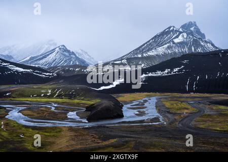 Eine atemberaubende Landschaft des isländischen Hochlands mit schneebedeckten Bergen, einem mäandernden Fluss und Kontrasten zwischen Schnee, Gras und Vulkanen Stockfoto