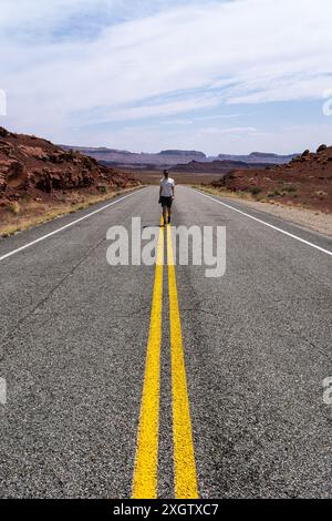 Ein einsamer Reisender steht auf einer einsamen Straße, die zur Hite Crossing Bridge führt, inmitten der malerischen Wüstenlandschaft des White Canyon im Glen Canyon N Stockfoto