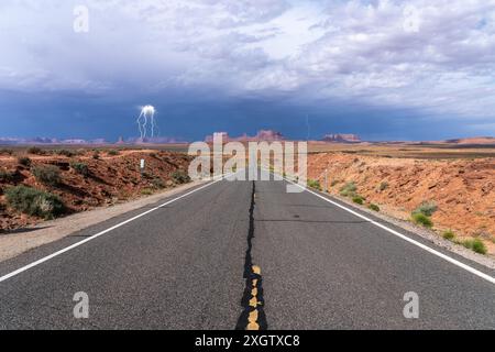 Ein beeindruckendes Bild, das ein Gewitter mit sichtbarem Blitz über dem berühmten Monument Valley von einem einsamen Abschnitt der Autobahn aus einfängt Stockfoto