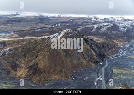 Ein Blick aus der Vogelperspektive auf Islands dramatische Landschaften mit schneebedeckten Bergen, verflochtenen Flusspfaden und einem beeindruckenden Kontrast zwischen den Stockfoto