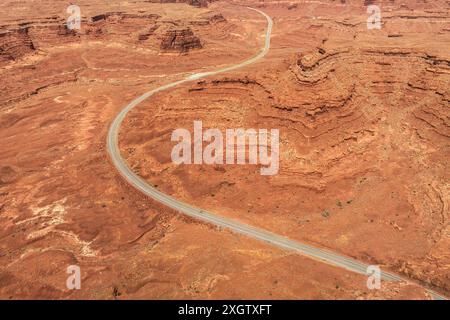 Die Aussicht auf eine einsame, gewundene Straße, die sich durch die zerklüftete, rote Landschaft des Valley of the Gods in Utah schlängelt, zeigt die krasse Natur Stockfoto