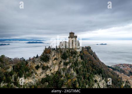Atemberaubende Aussicht auf den ersten Guaita-Turm auf der Burg San Marino, die auf einer Klippe liegt, umgeben von einem Meer aus Wolken und fernen Hügeln Stockfoto