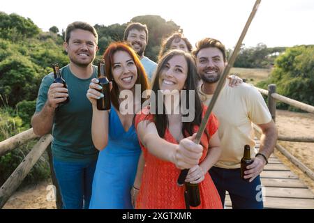 Eine Gruppe von Freunden mit Bier in der Hand, versammelte sich draußen bei Sonnenuntergang, während sie ein Selfie machten, um Freude und Nähe zu zeigen, ohne ihre Identi zu enthüllen Stockfoto