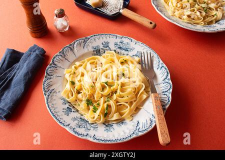 Eine Nahaufnahme von Fettuccine Alfredo auf rotem Hintergrund. Garniert mit frischer Petersilie und geriebenem Parmesankäse Stockfoto