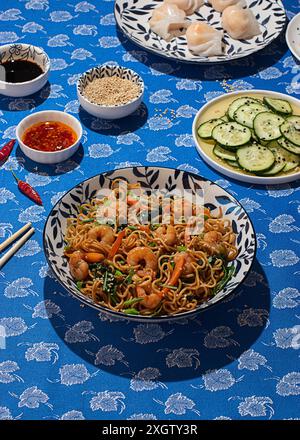 Blick von oben auf einen lebhaften Tisch mit chinesischer Küche, mit gebratenen Nudeln mit Garnelen und Gemüse in einer traditionellen dekorativen Schüssel, umgeben Stockfoto