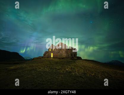 Eine eindringlich schöne Szene mit einem verlassenen Haus, das in das gespenstische Grün der Nordlichter getaucht ist, unter einem Sternenhimmel in der isländischen Wildnis Stockfoto
