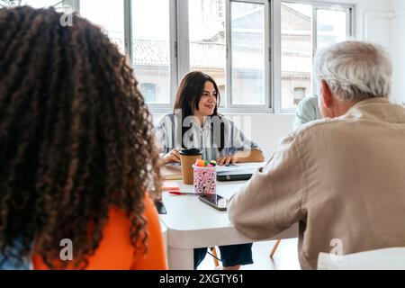 Eine multiethnische Gruppe von Fachleuten führt eine gemeinsame Diskussion im Coworking Space. Frauen und ältere Männer teilen Ideen und zeigen eine Vielfalt Stockfoto