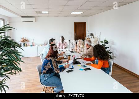 Ein multiethnisches Team arbeitet dynamisch in einem Coworking-Raum zusammen, der von Gadgets und Technologie umgeben ist. Einzelpersonen aus Afrika, Kaukasiern, Stockfoto