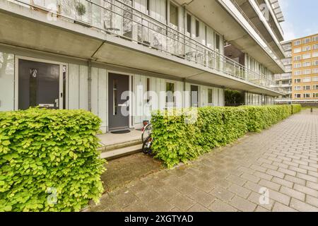 Moderner Wohnblock mit Türen im Erdgeschoss, großen Balkonen und lebhaften grünen Büschen in Henkenshage, Amsterdam, Niederlande Stockfoto