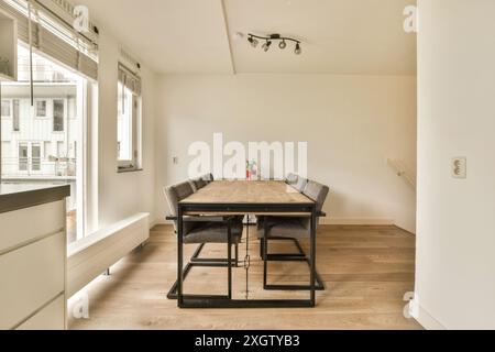 Dieser moderne Speisesaal in Henkenshage, Amsterdam, verfügt über einen großen Holztisch mit Metallakzenten, umgeben von eleganten Stühlen, die in natura getaucht sind Stockfoto