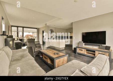 Dieses Bild zeigt ein modernes Wohnzimmer, das nahtlos mit einer offenen Küche verbunden ist, mit eleganten Möbeln und neutralen Farben. Stockfoto