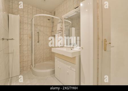 Dieses gemütliche Badezimmer in Poststraat, Niederlande, bietet moderne Annehmlichkeiten wie eine geschwungene Duschkabine, einen eleganten weißen Kosmetikbereich und Beige Stockfoto