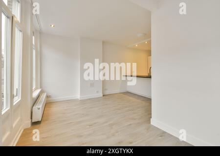 Ein leeres Wohnzimmer mit Holzfußboden und weißen Wänden auf beiden Seiten des Zimmers, es gibt ein großes Fenster Stockfoto