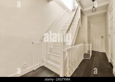 Die gut beleuchtete Inneneinrichtung verfügt über eine klassische weiße Treppe mit einem modernen Sicherheitstor, ergänzt durch dunkle Holzböden und neutrale Farbtöne. Stockfoto