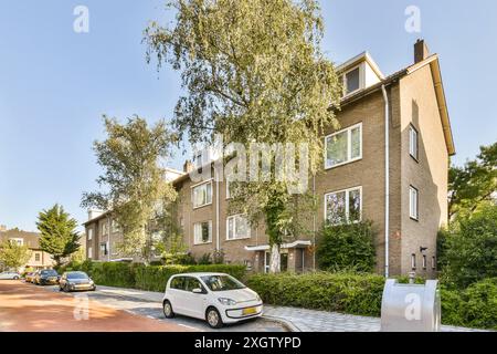 Ein modernes mehrstöckiges Wohnhaus aus Backstein an einem sonnigen Tag mit grüner Umgebung und geparkten Autos. Stockfoto