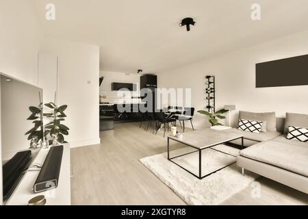Modernes minimalistisches Wohnzimmer mit offener Küche, großem weißen L-förmigen Sofa, Essbereich und viel Tageslicht Stockfoto