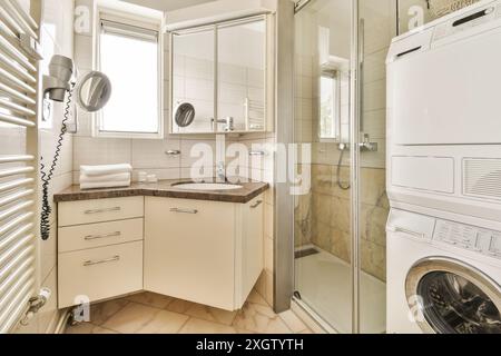 Kompaktes, modernes Badezimmer mit Kosmetikbereich, Dusche und eingebauter Waschmaschine, gefliesten Wänden und Tageslicht. Stockfoto