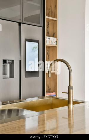 Eine elegante, moderne Küche mit elegantem Messinghahn, Edelstahlwaschbecken und Holzregalen. Stockfoto