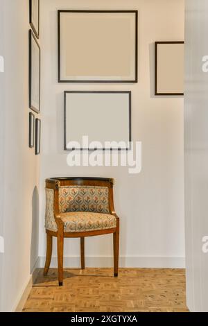 Ein Vintage-Polsterstuhl steht vor einer leeren Wand mit leeren Bilderrahmen in einer modernen Inneneinrichtung. Stockfoto