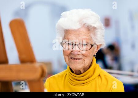 Eine ältere Frau mit weißem Haar und Brille, gekleidet in einem leuchtend gelben Oberteil, zeigt ein warmes und sanftes Lächeln, das einen fröhlichen und aktiven lebensstil darstellt Stockfoto