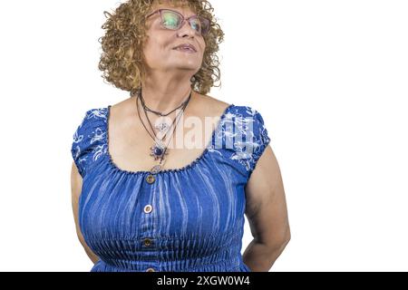 Das Bild zeigt eine 60-jährige Frau, die vor weißem Hintergrund steht. Sie trägt eine blaue Rüschenbluse Stockfoto