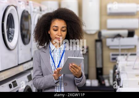 Junge professionelle Frau, die in einem Geräteschäft steht und ein digitales Tablet für die Bestandsverwaltung verwendet. Konzept von Einzelhandel, Technologie, Kundenservice und Geschäftsbetrieb. Stockfoto