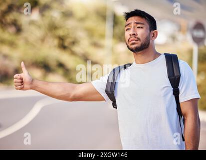 Asiatischer Mann, Straße und verzweifelt mit Daumen hoch zum Trampen für eine Fahrt oder Heimreise in Kalifornien. Mann, Rucksack und traurig oder müde mit Stockfoto