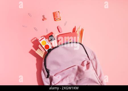 Lila Rucksack mit Schulutensilien vor rosa Hintergrund Stockfoto