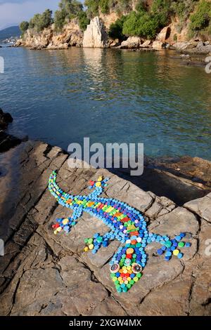 Gecko-Design auf Küstenfelsen aus Flaschenaufsätzen und Zigarettenanzündern, die an Stränden in Milina, South Pelion, Griechenland gesammelt wurden Stockfoto