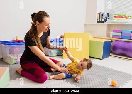 Physiotherapeut arbeitet mit einem Kind mit schlechtem Muskeltonus während der neurologischen Säuglingsuntersuchung im Therapieraum. Neurologische Rehabilitation Stockfoto