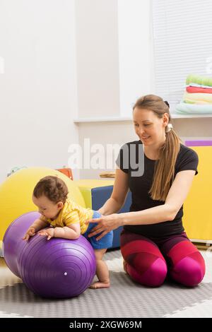 Kind, das sich in Physiotherapie bei ZNS-Erkrankungen im Rehabilitationszentrum einsetzt. Kleinkind, das Übungen auf einem Therapieball mit Assistenzarzt macht Stockfoto