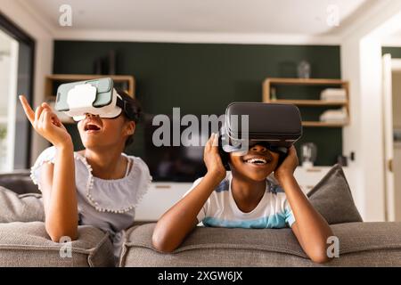 Bruder und Schwester im Teenageralter genießen VR-Headsets zu Hause. Sie tauchen in eine virtuelle Realität ein und teilen einen Moment voller Spaß und Entdeckungen Stockfoto