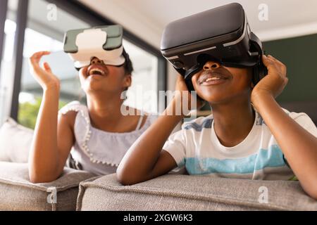 Bruder und Schwester im Teenageralter genießen VR-Headsets zu Hause. Sie tauchen in eine virtuelle Realität ein und sitzen bequem auf einer Couch. Stockfoto