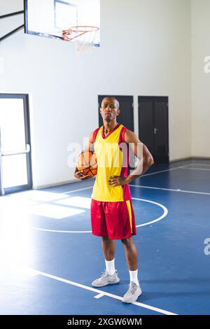 Ein Afroamerikaner steht selbstbewusst auf einem Basketballfeld und verkörpert einen sportlichen Lebensstil. Seine Basketballuniform deutet darauf hin, dass er bereit für ein Spiel ist Stockfoto