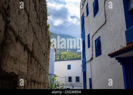 Blick von der engen Gasse auf die Moschee auf dem Hügel in der Ferne. Marokko. Die Häuser in Blau- und Weißtönen sind traumhaft und charmant. Chefchao Stockfoto