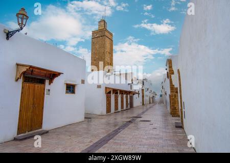 Weiß getünchte Gasse in Kasbah von Udayas unter klarem Himmel. In der Ferne steht ein markanter Turm. Architektonische Details spiegeln den Ursprung der Berber-Verteidigung wider Stockfoto